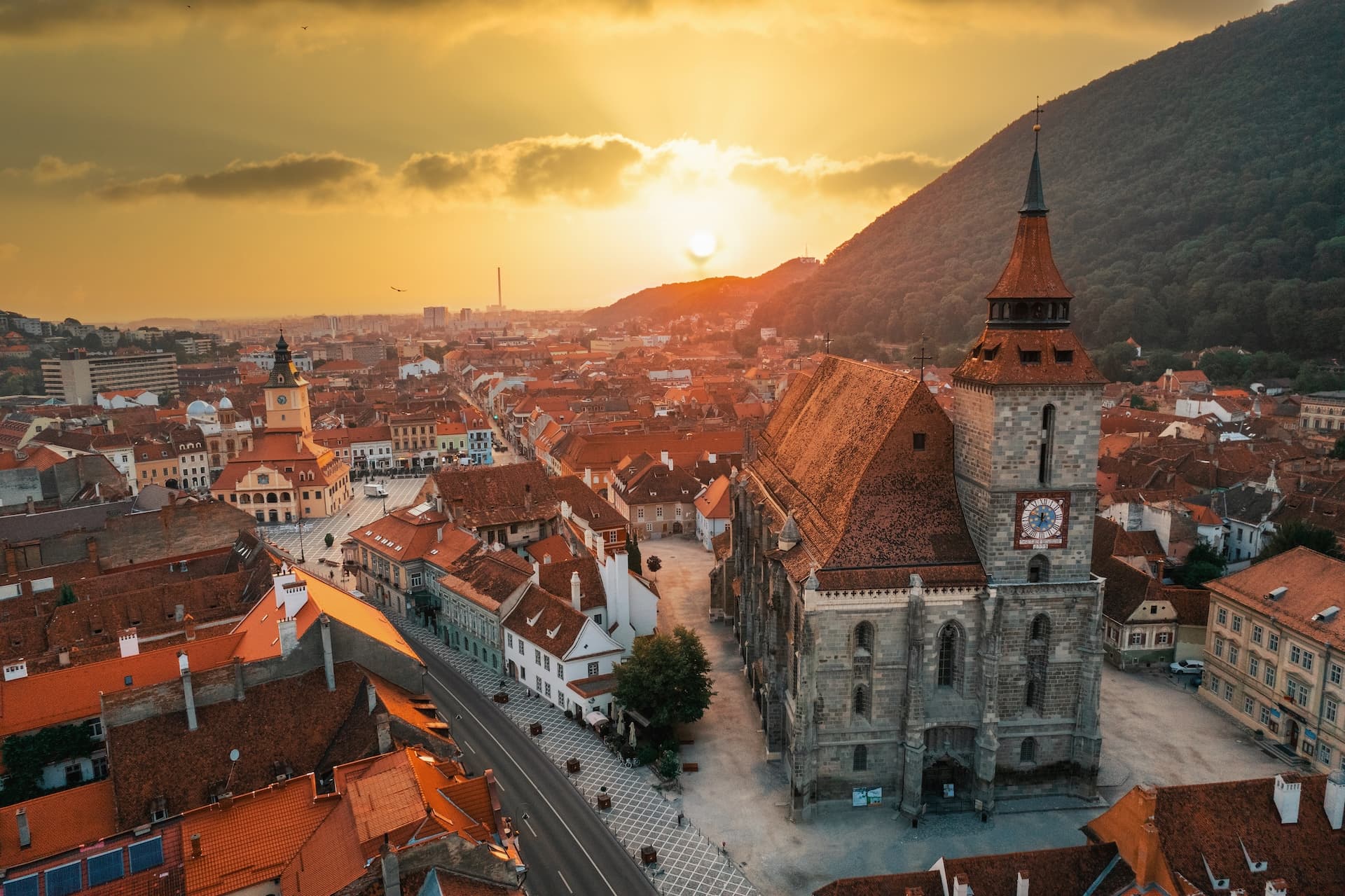 Black Church in Brasov, Romania, at sunset overlooking terracotta roofs and a forested mountain.