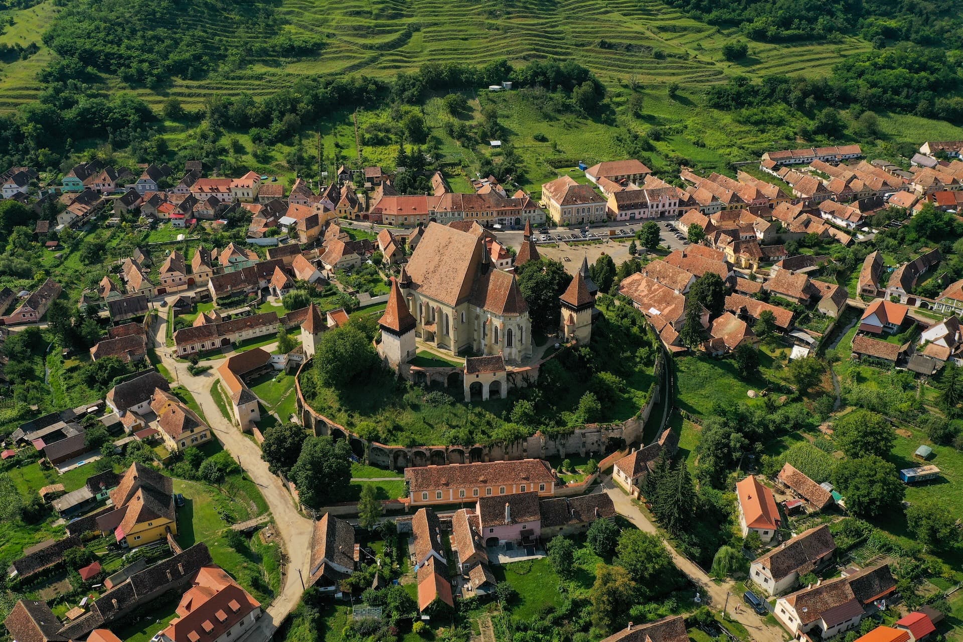 Aerial view of fortified church and village with red roofs surrounded by green hills in Biertan, Romania.