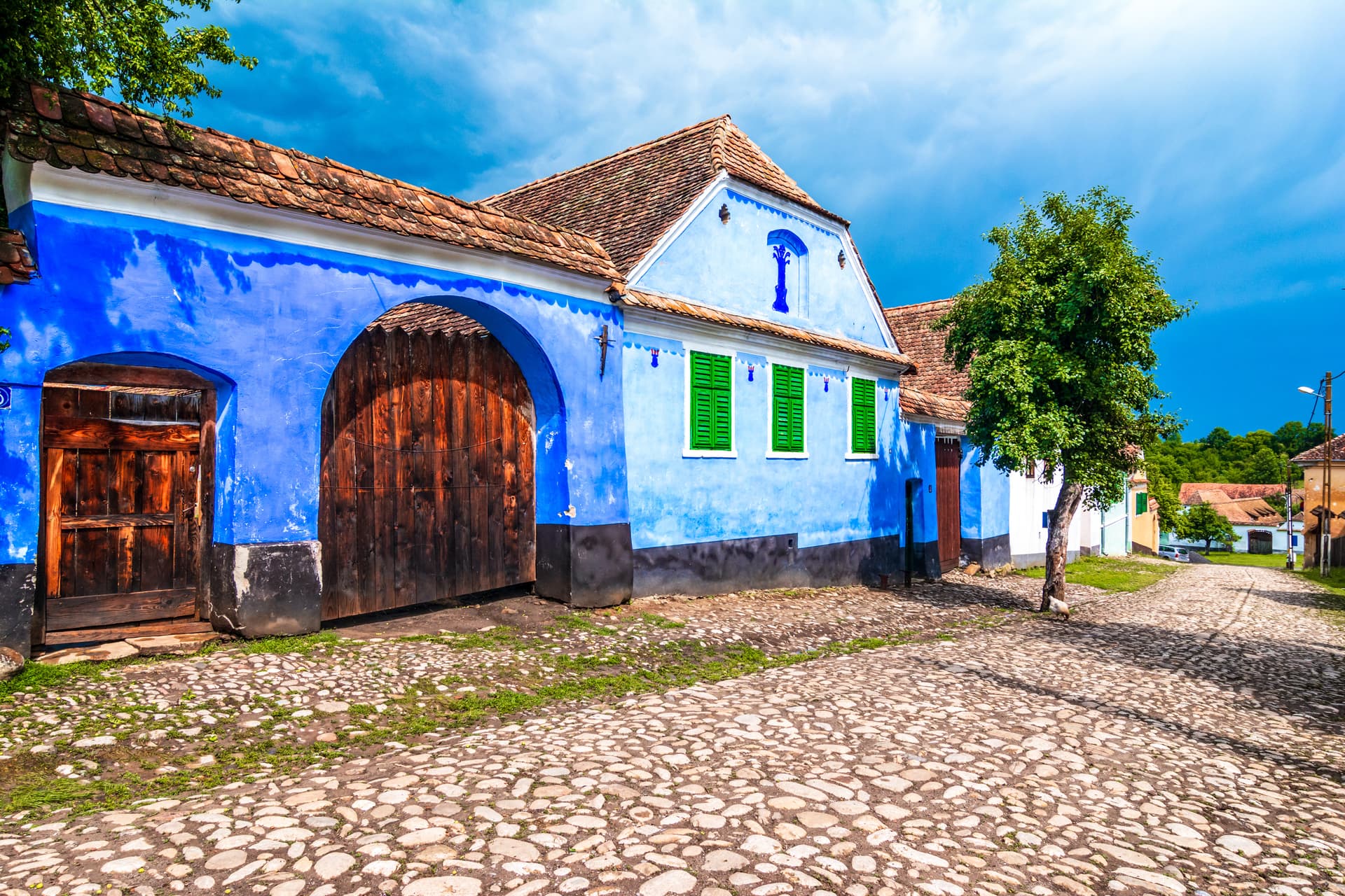Blue-painted traditional house with wooden gate and green shutters on cobblestone street in Viscri.