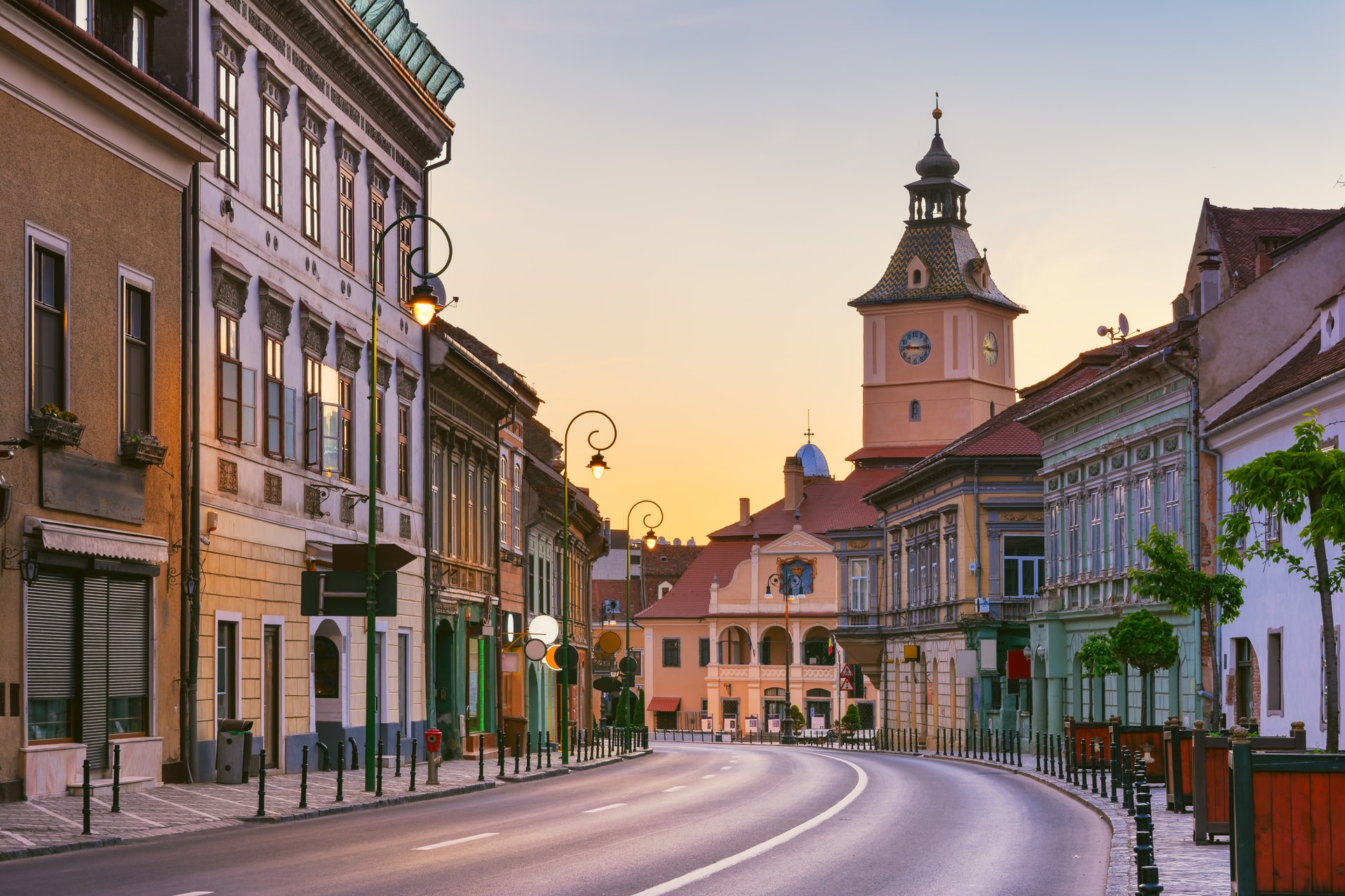 Street curving past historic buildings toward a clock tower at sunset in Brasov, Romania.