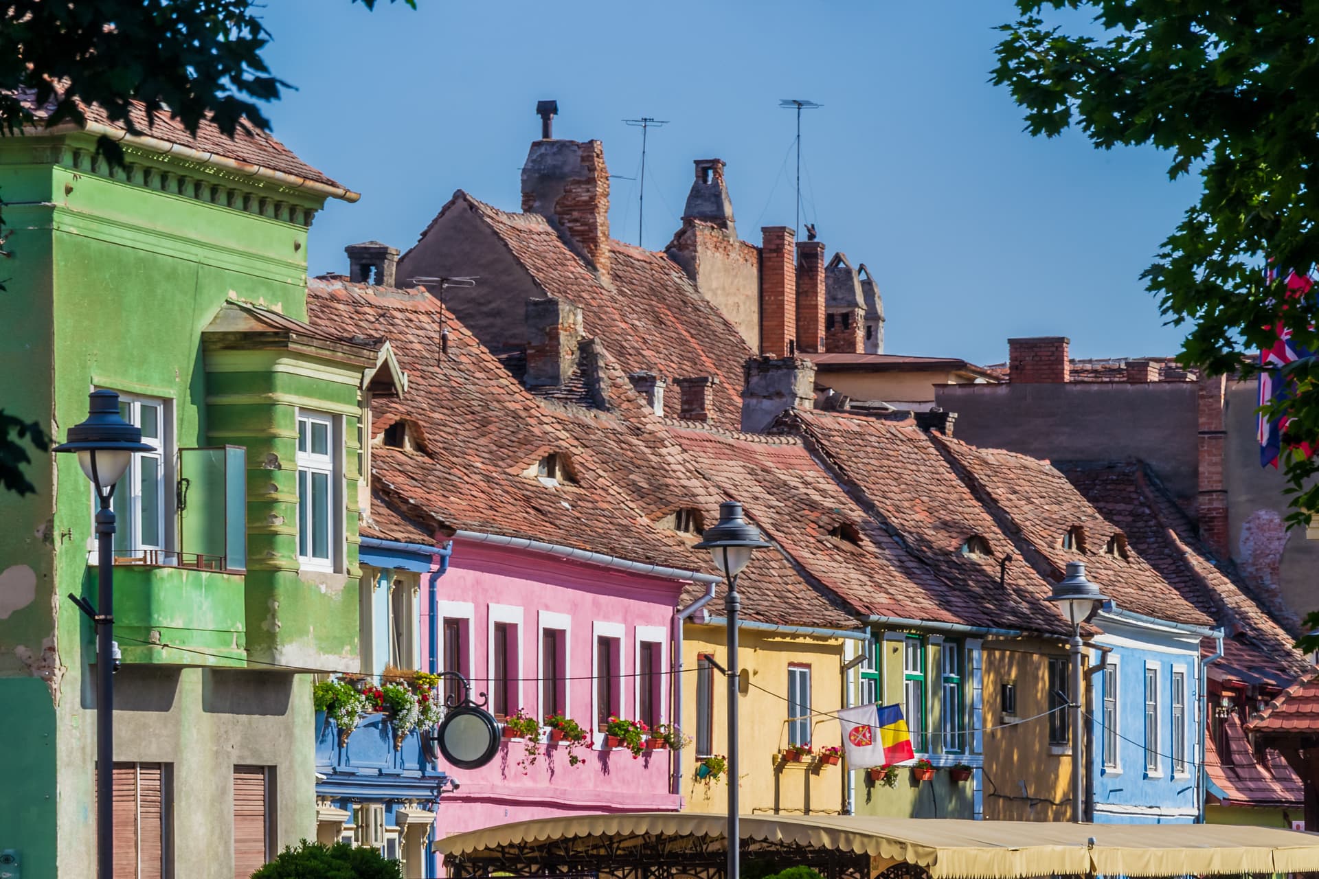 Colorful pastel houses with terracotta roofs and chimneys under a clear blue sky in Sibiu, Romania.