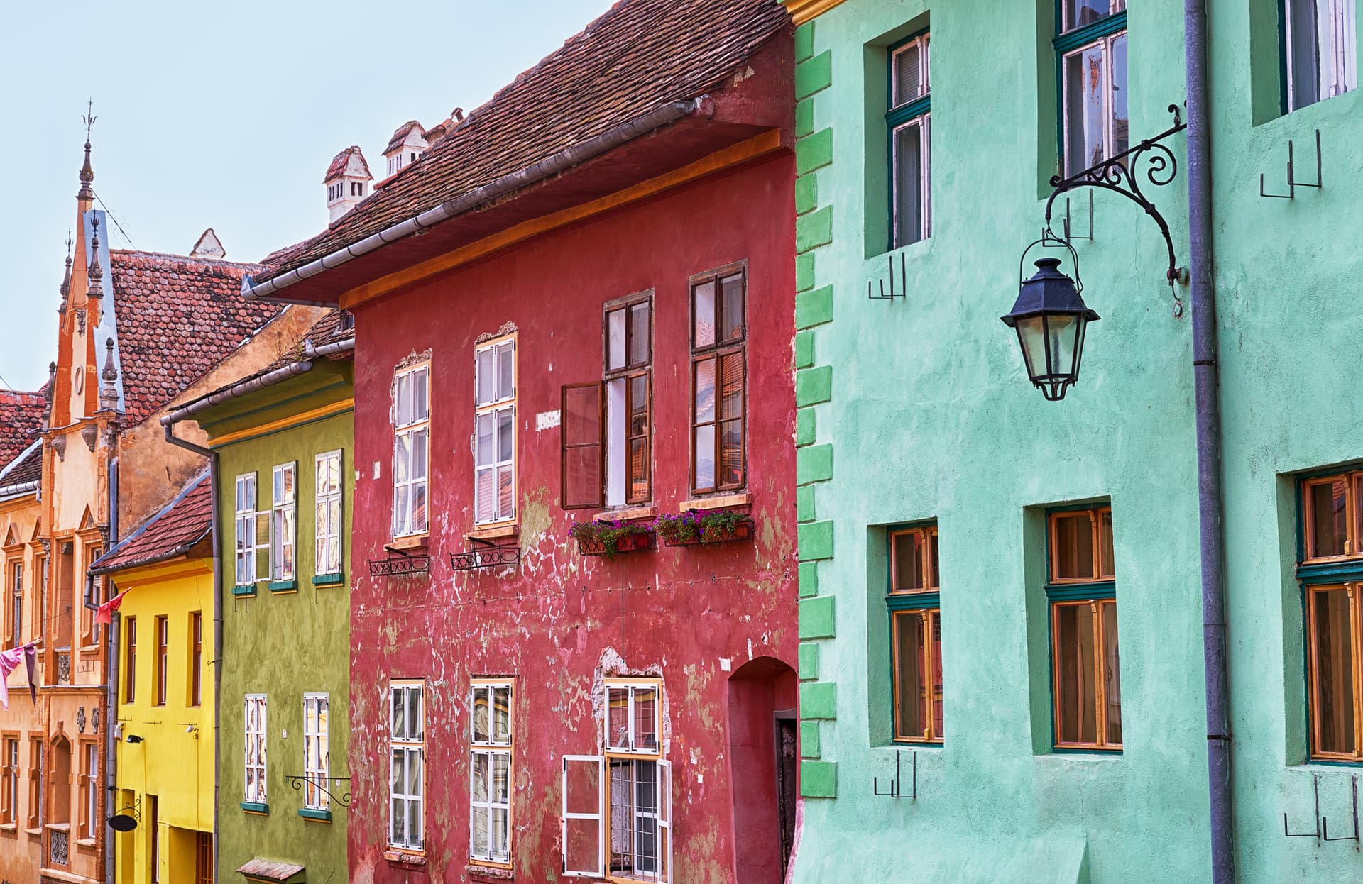 Colorful historic facades in Sighisoara, Romania, featuring red, green, and yellow buildings with tiled roofs.