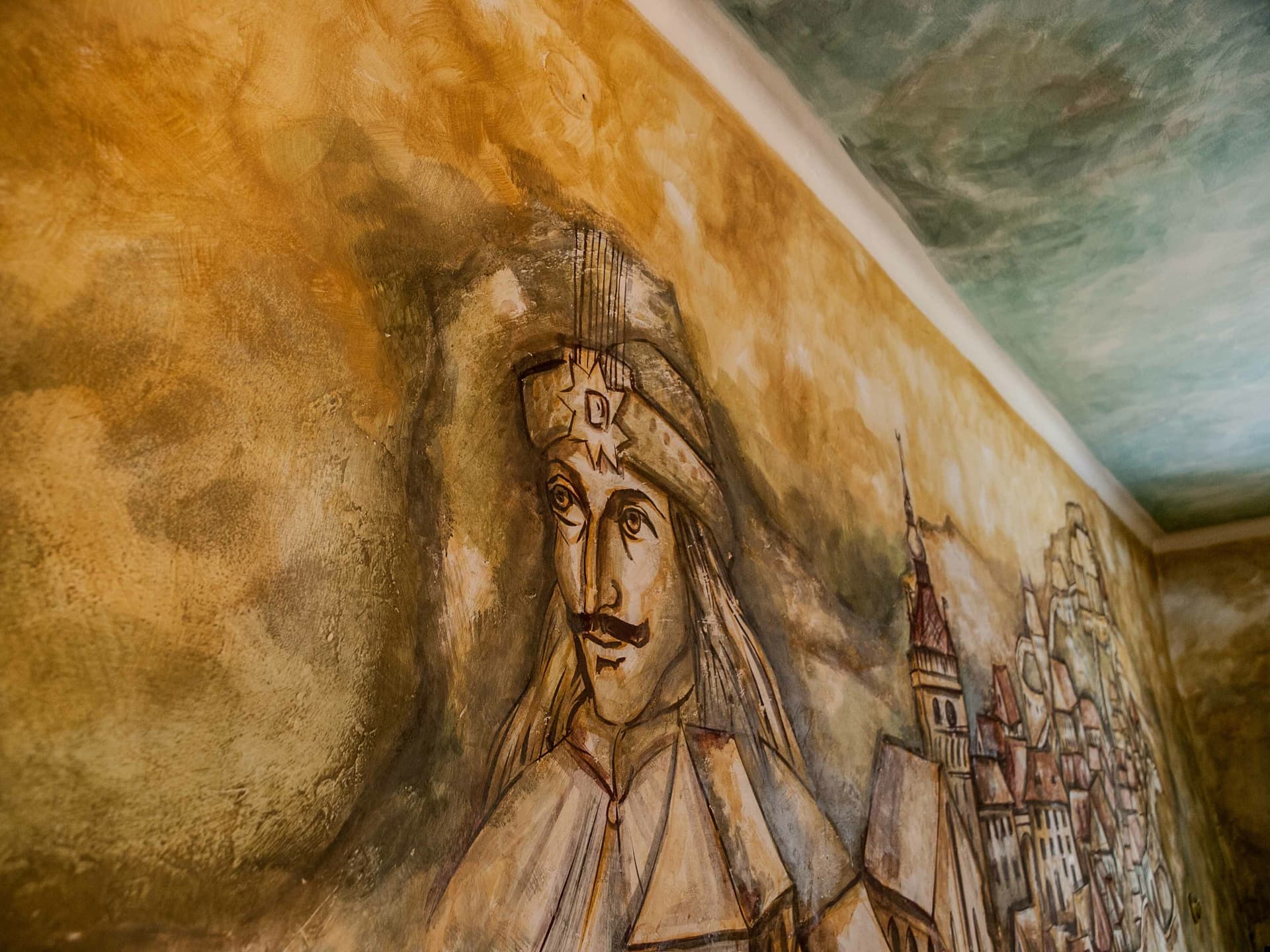 Mural painting of Vlad the Impaler portrait next to a historic European townscape.